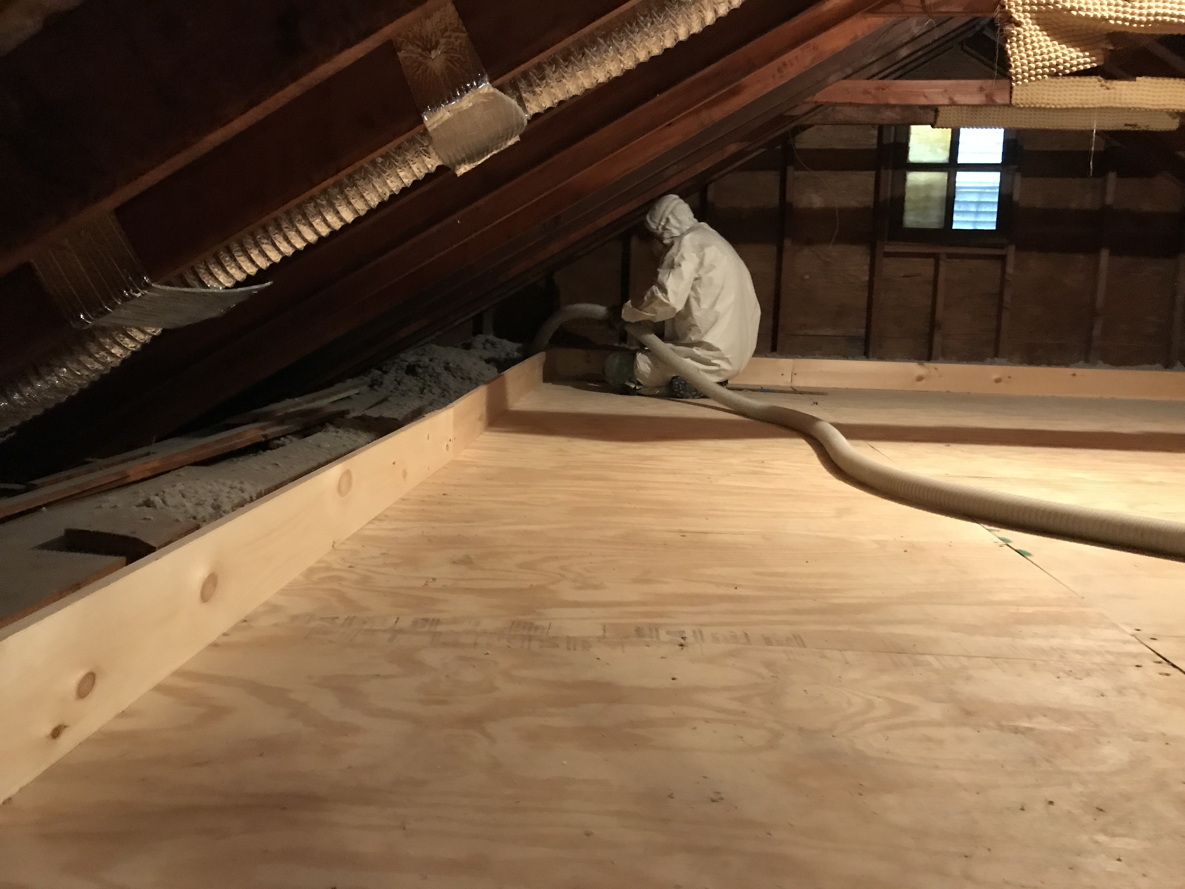 An installer adds loose-fill insulation beside an attic platform.
